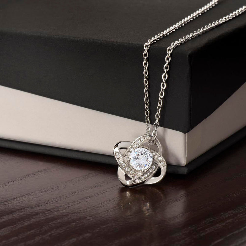 Silver love knot pendant on a fine chain, resting on a dark surface