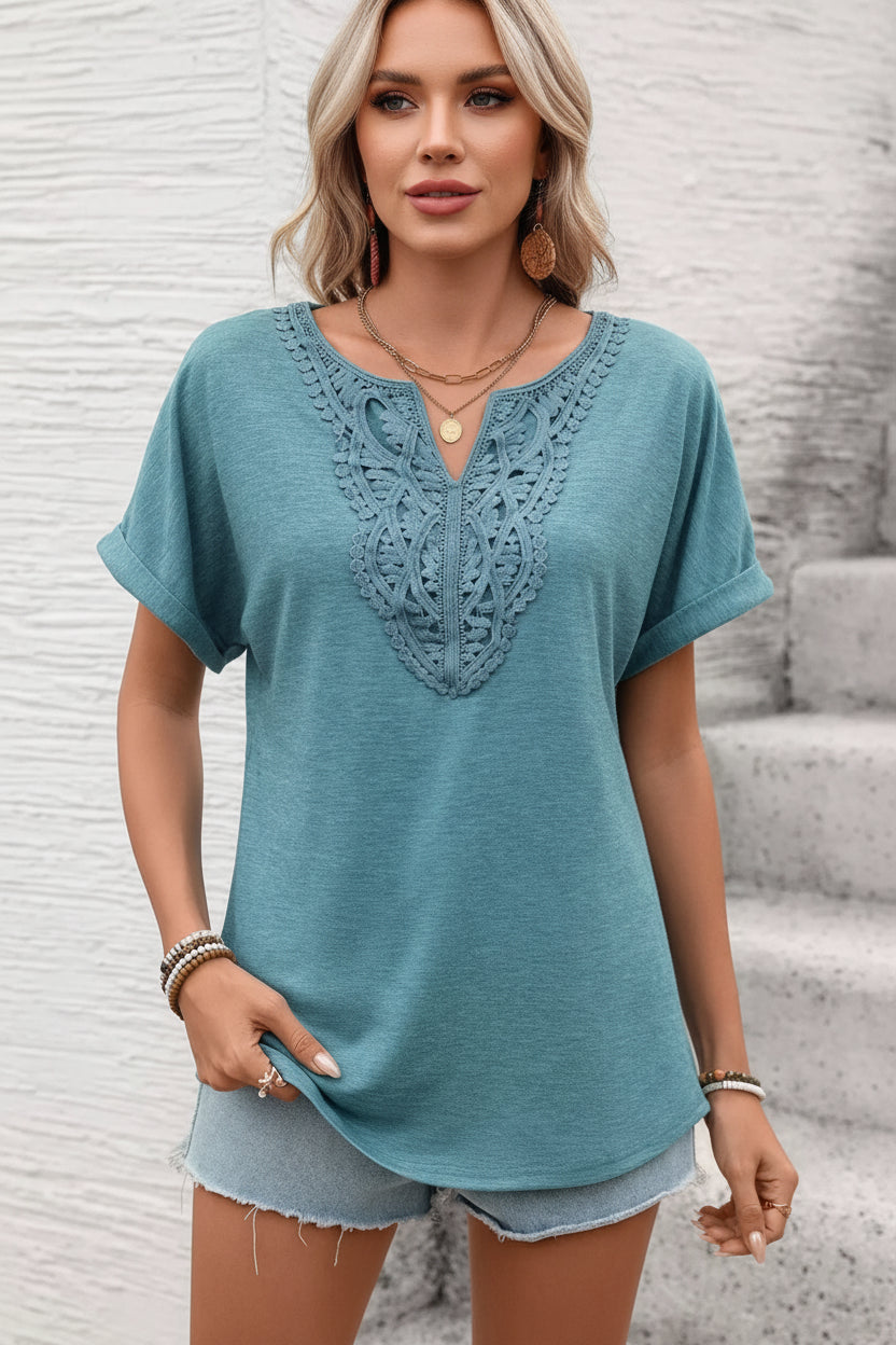 Woman wearing a teal short-sleeve top with lace detailing against a light background
