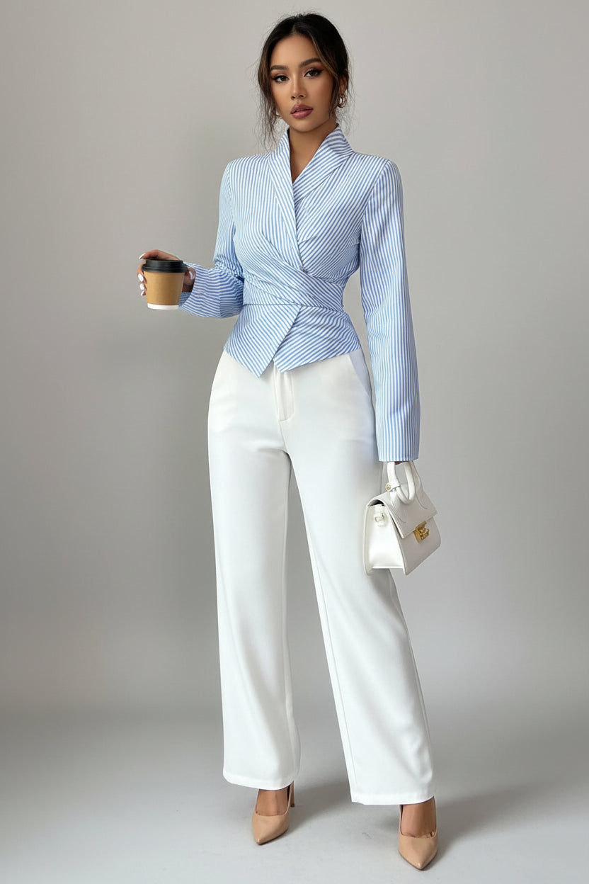 A woman wearing a light blue and white vertically striped wrap-style blazer with long sleeves, paired with white pants, holding a coffee cup against a plain light gray background.