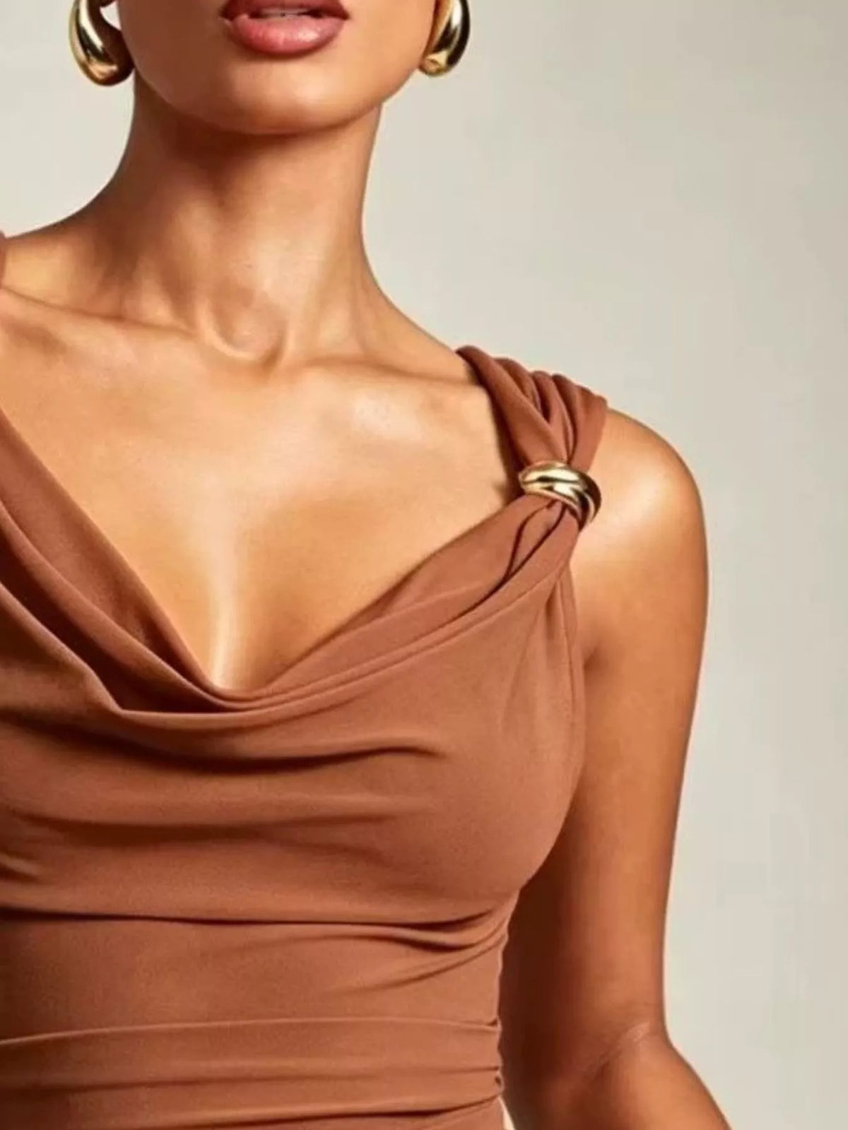 Close-up of a person wearing a brown dress with a gold detail on a neutral background