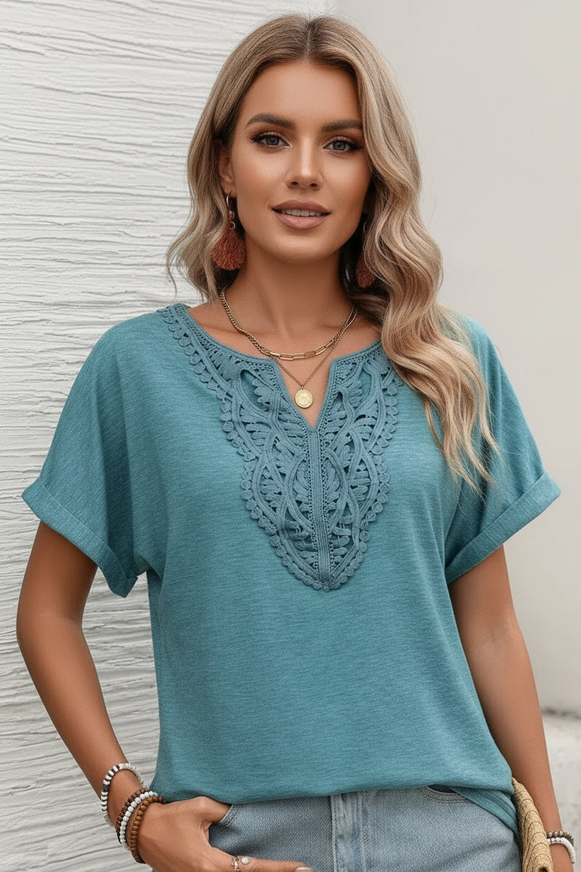 Woman wearing a teal top with lace detail and denim shorts against a neutral background