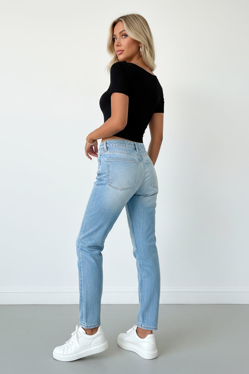 Person wearing a black top and light blue jeans against a neutral background
