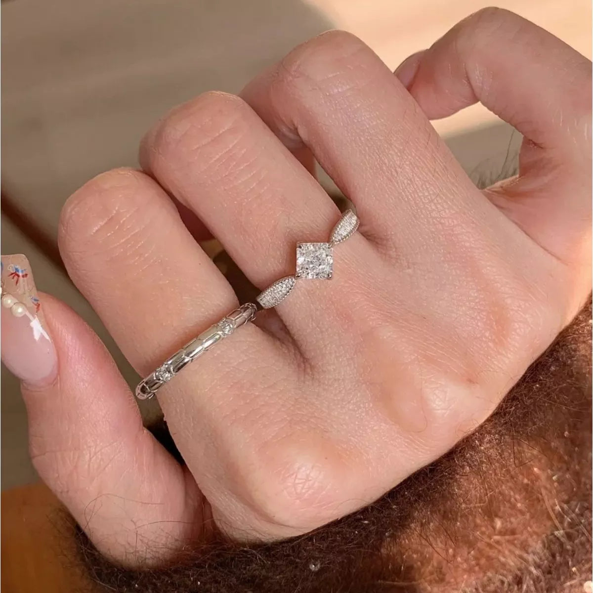 Close-up of a hand wearing two diamond rings on a neutral background