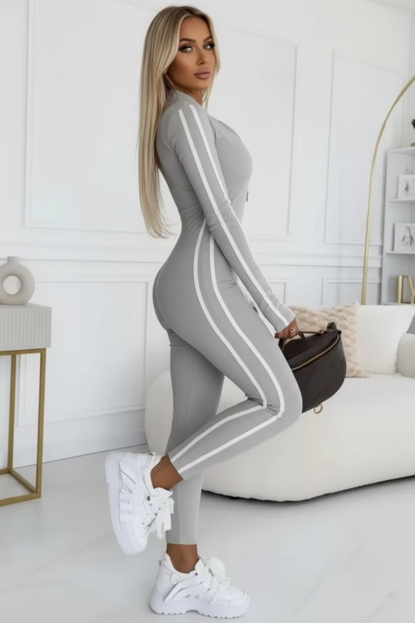 Person wearing a gray tracksuit with white stripes, sitting on a white couch.