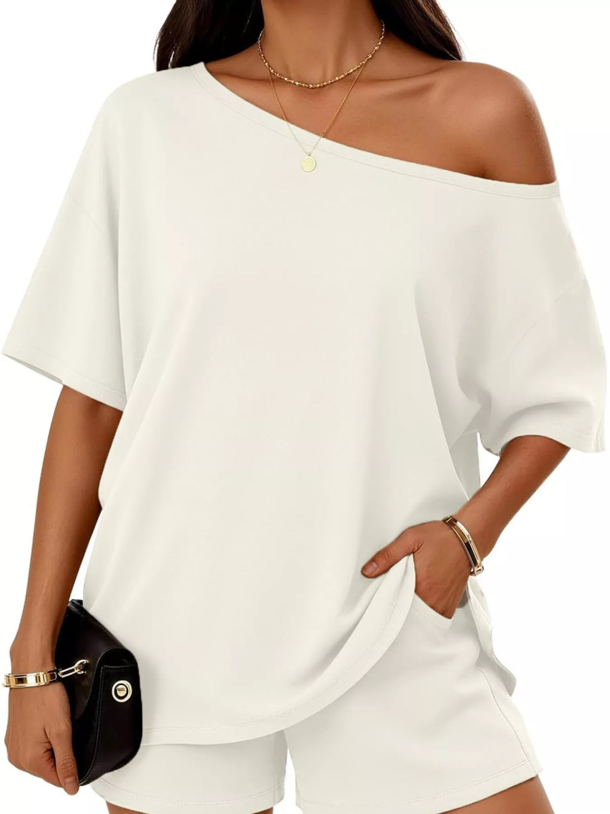 Woman wearing a white off-shoulder top and shorts set with a black clutch.