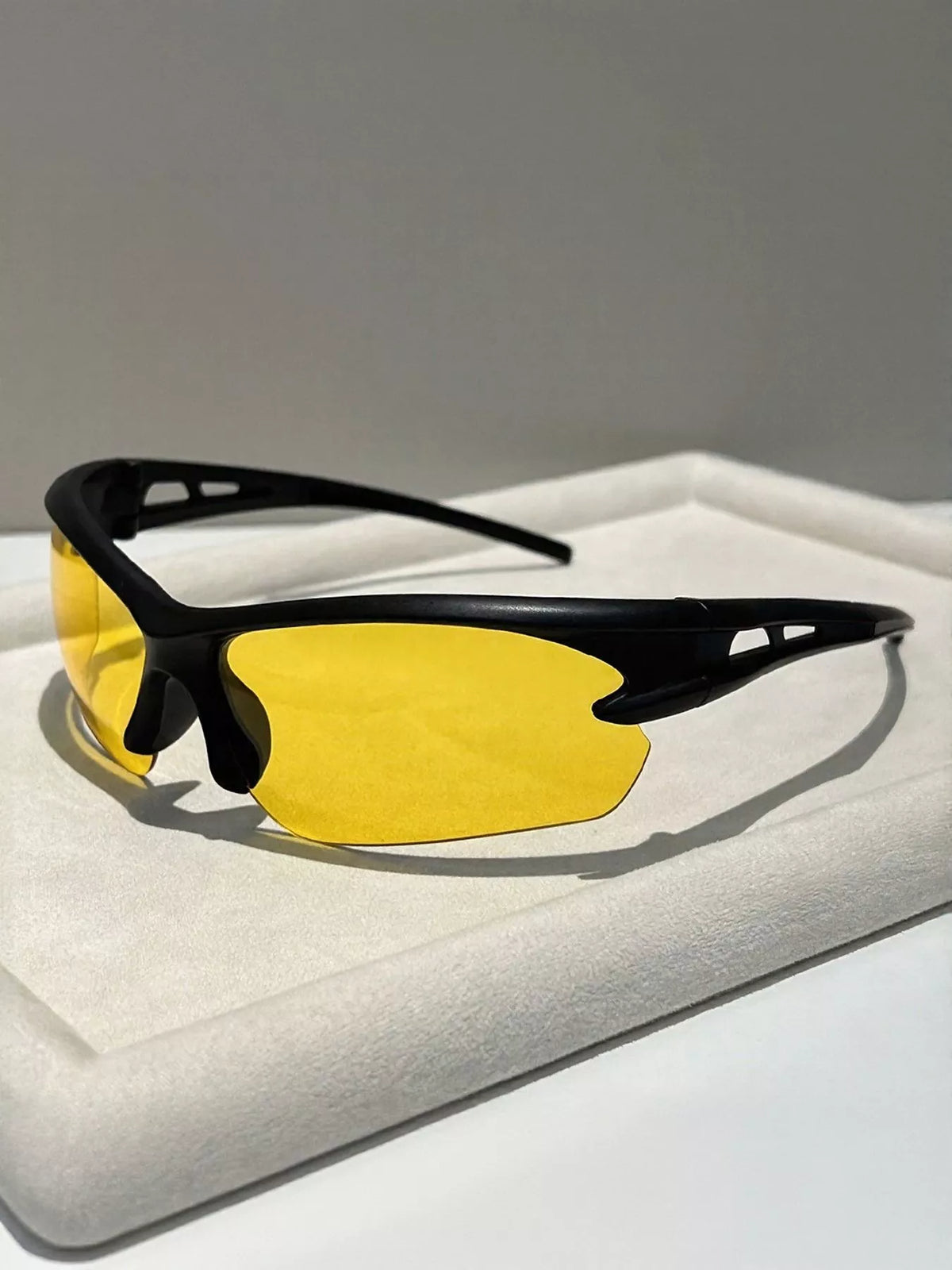 Sunglasses with yellow lenses and black frames on a light gray surface
