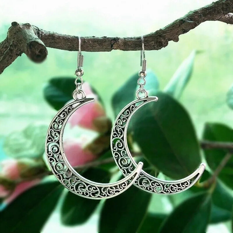 Silver crescent moon earrings hanging on a branch with green leaves in the background