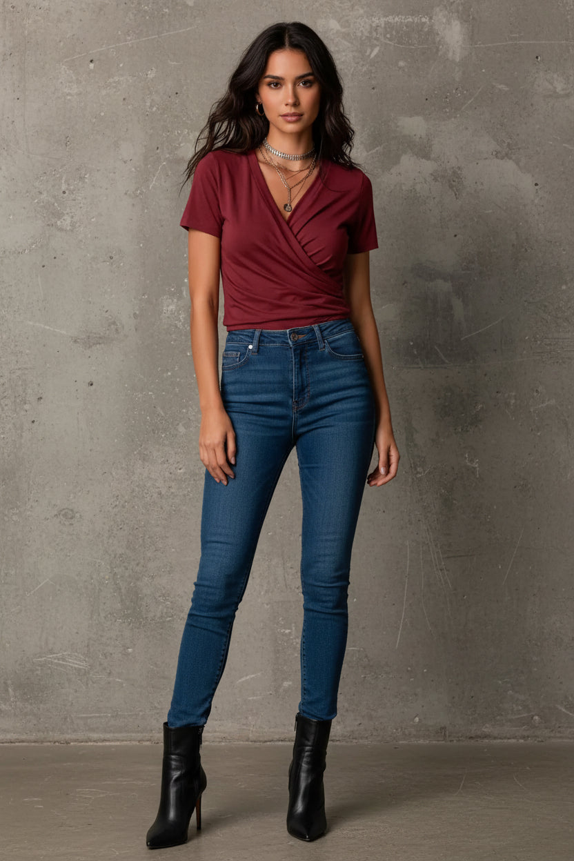 A close-up of a woman wearing a short-sleeve wrap-style V-neck top in burgundy, styled with layered silver necklaces.