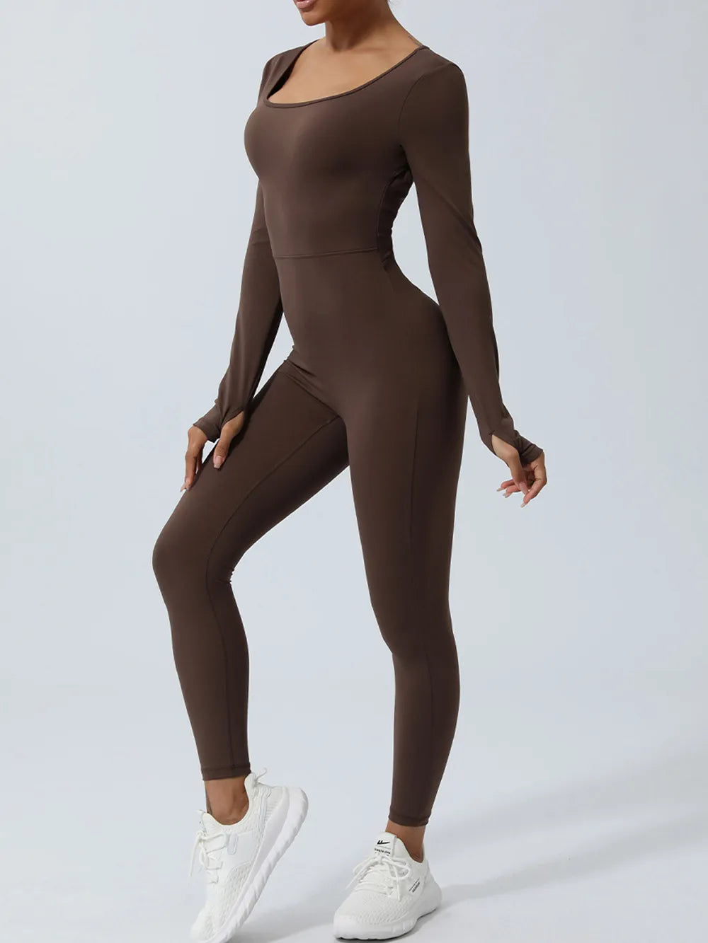 One knee lifted forward in the brown jumpsuit, long sleeves pulled down over the hands