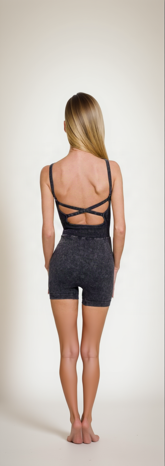 Rear view of the washed black romper, crisscross straps over an open back, barefoot
