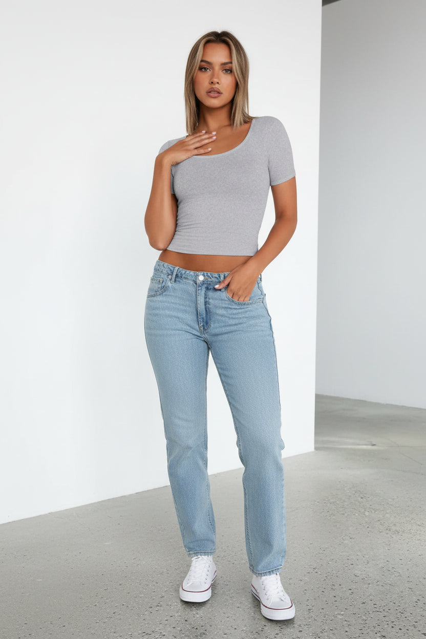 Person wearing a gray crop top and blue jeans against a white background