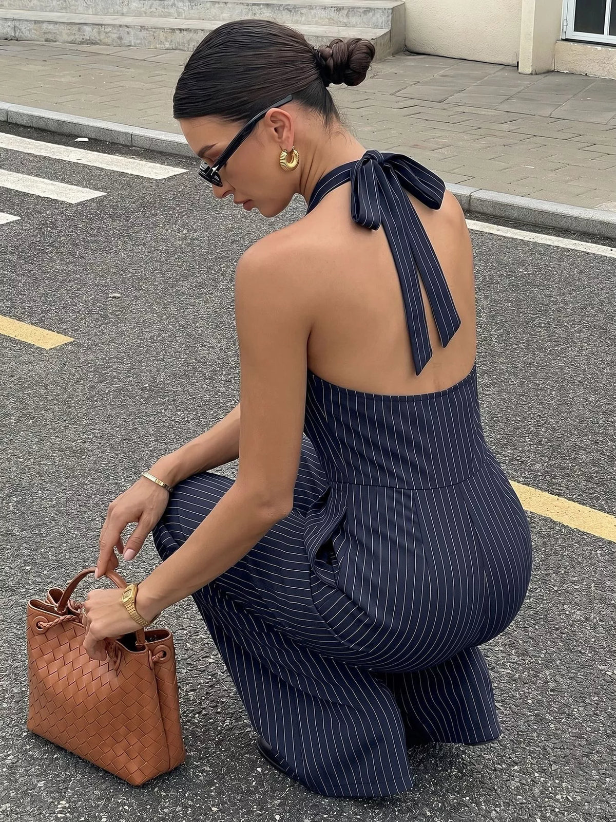 Woman in a navy pinstripe jumpsuit holding a brown handbag on a street.