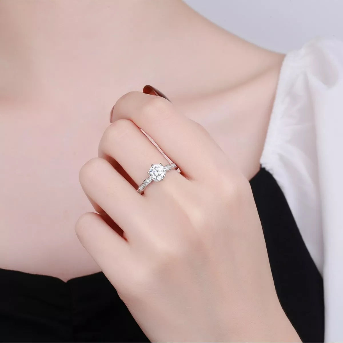 Silver ring with a diamond on a person's finger against a neutral background