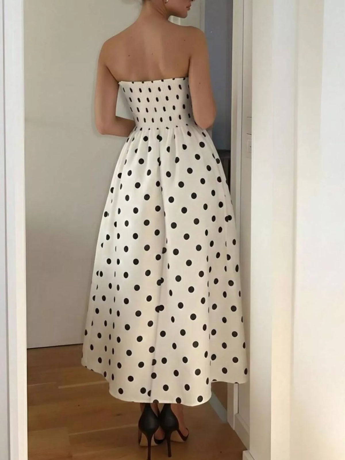 Woman wearing a white strapless dress with black polka dots, standing in a room.