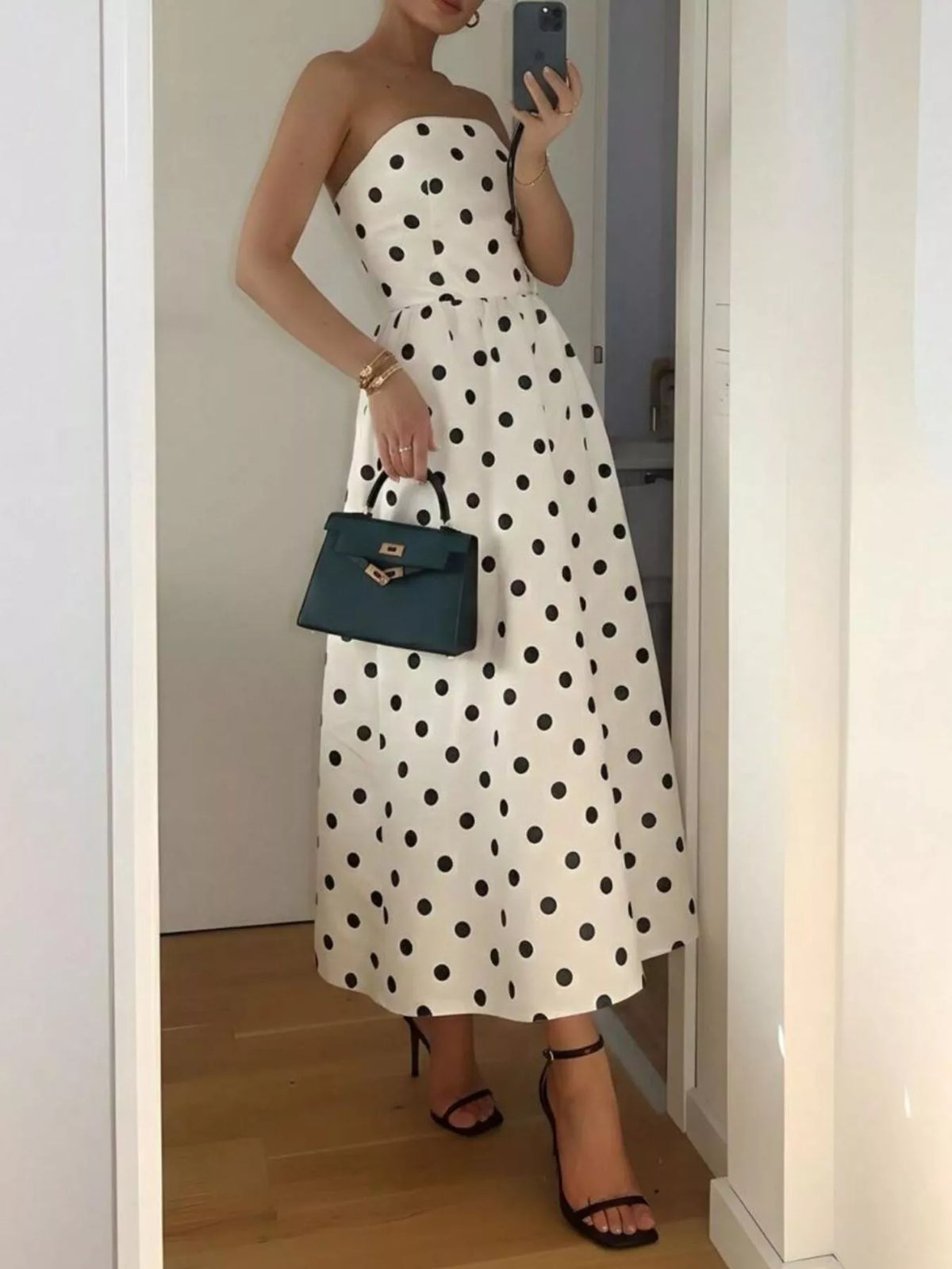 Person wearing a strapless polka dot dress holding a blue handbag.