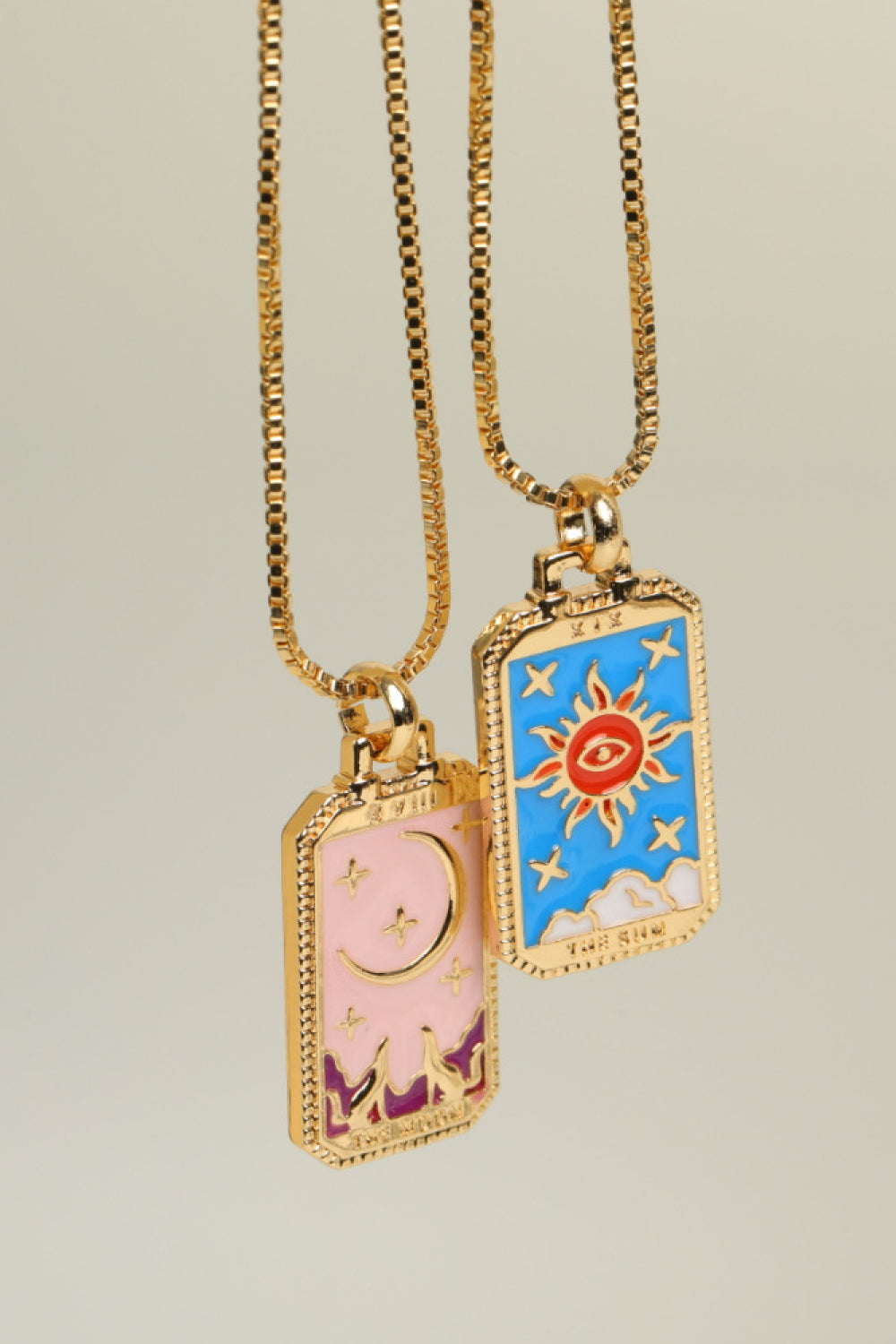 Two gold necklaces with colorful pendants on a beige background
