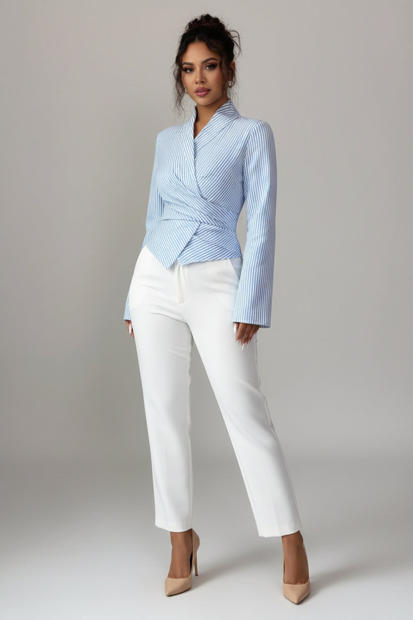 A woman wearing a light blue and white vertically striped wrap-style blazer with long bell sleeves and a tied waist, paired with white pants, against a plain light gray background.