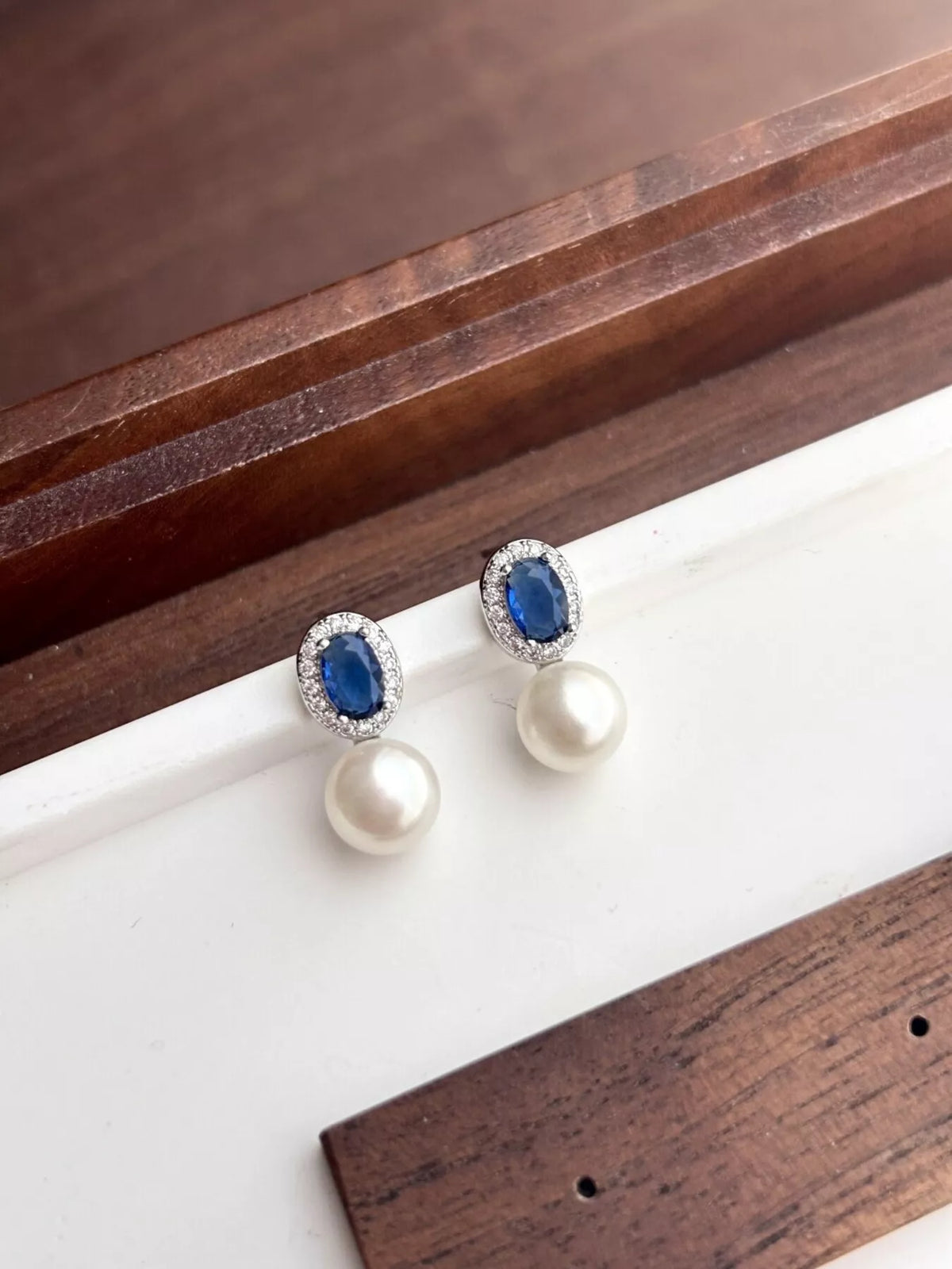 Pearl and sapphire earrings on a wooden surface