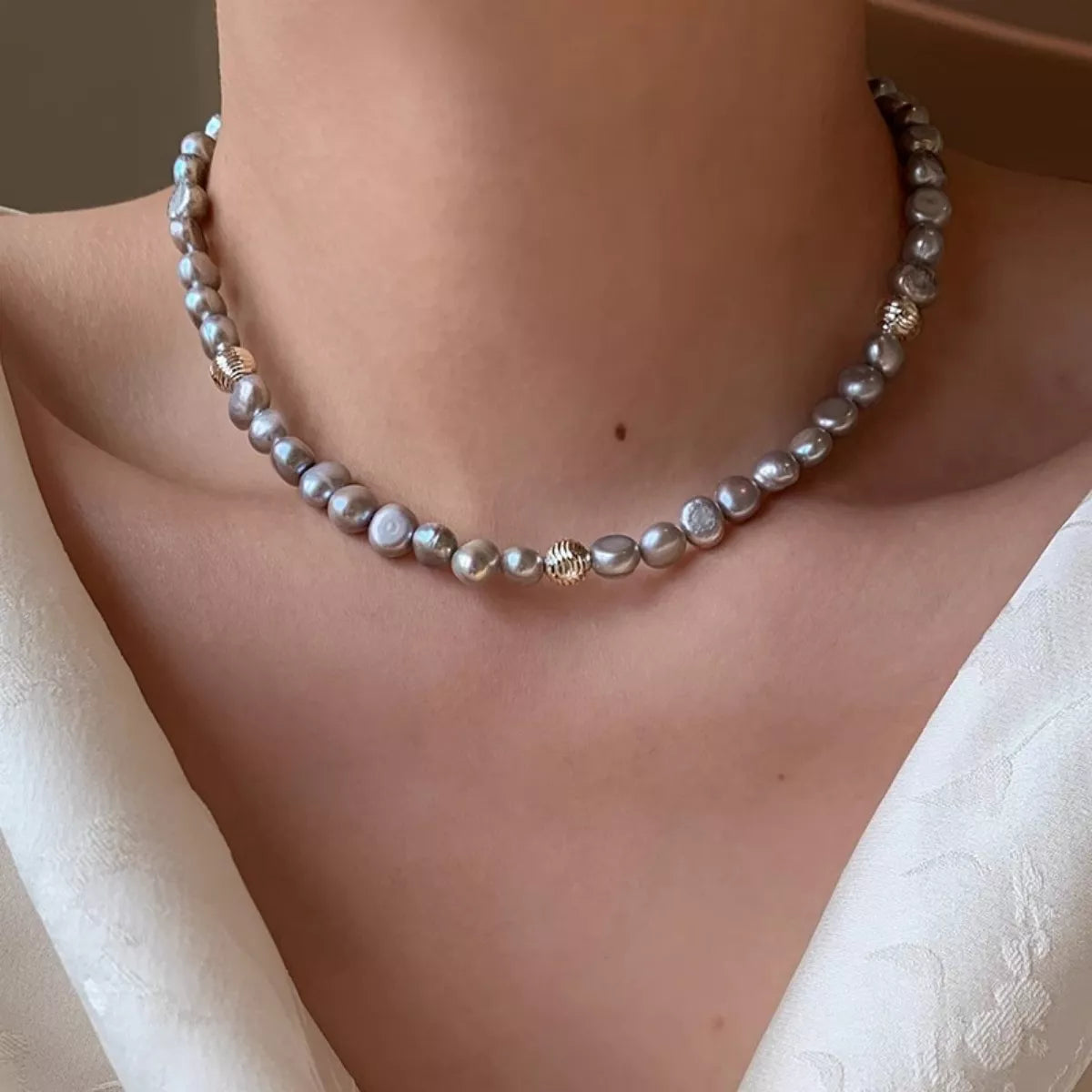 Pearl necklace being worn on a person's neck with a neutral background