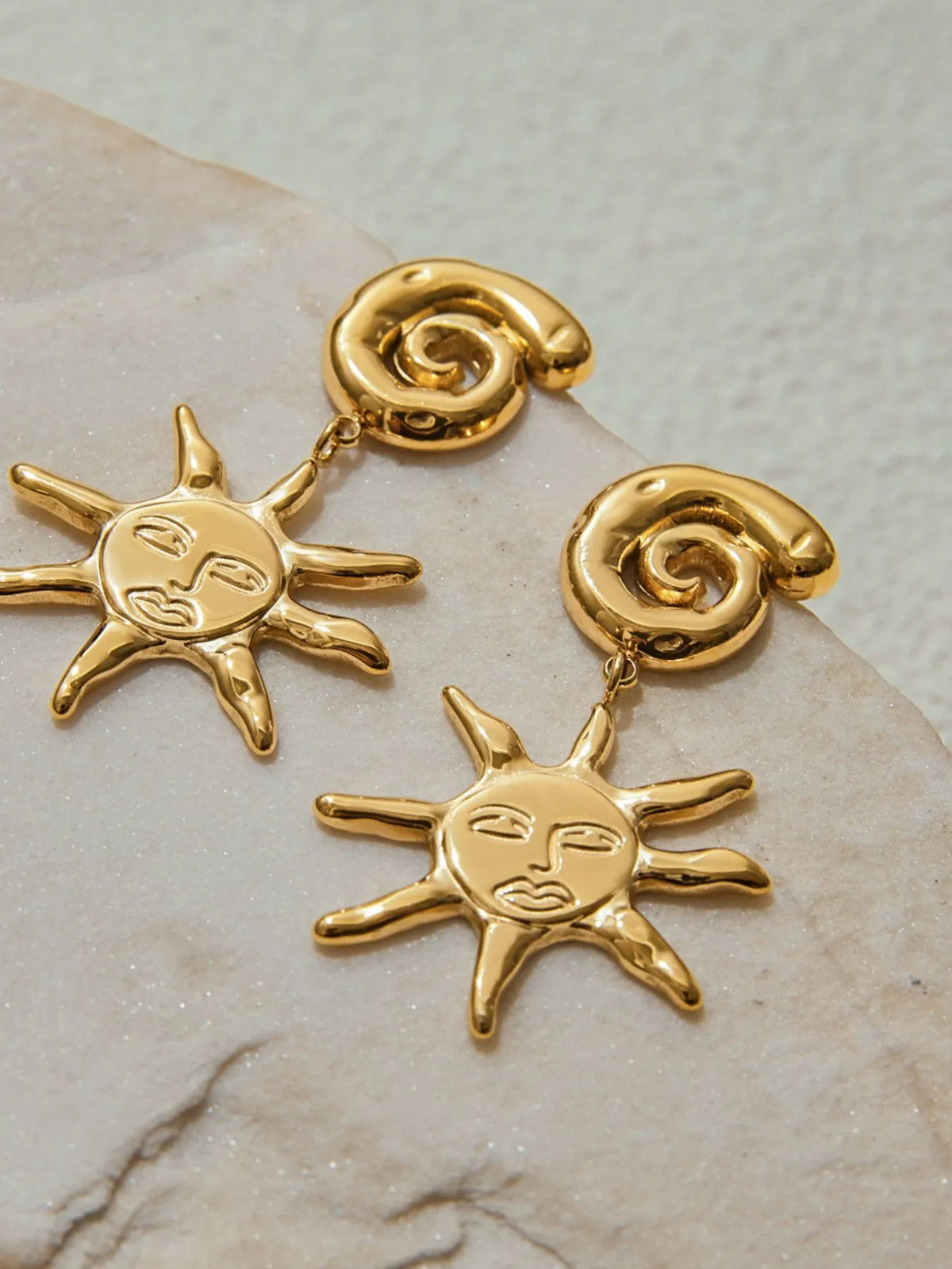 Gold sun-shaped earrings on a marble surface