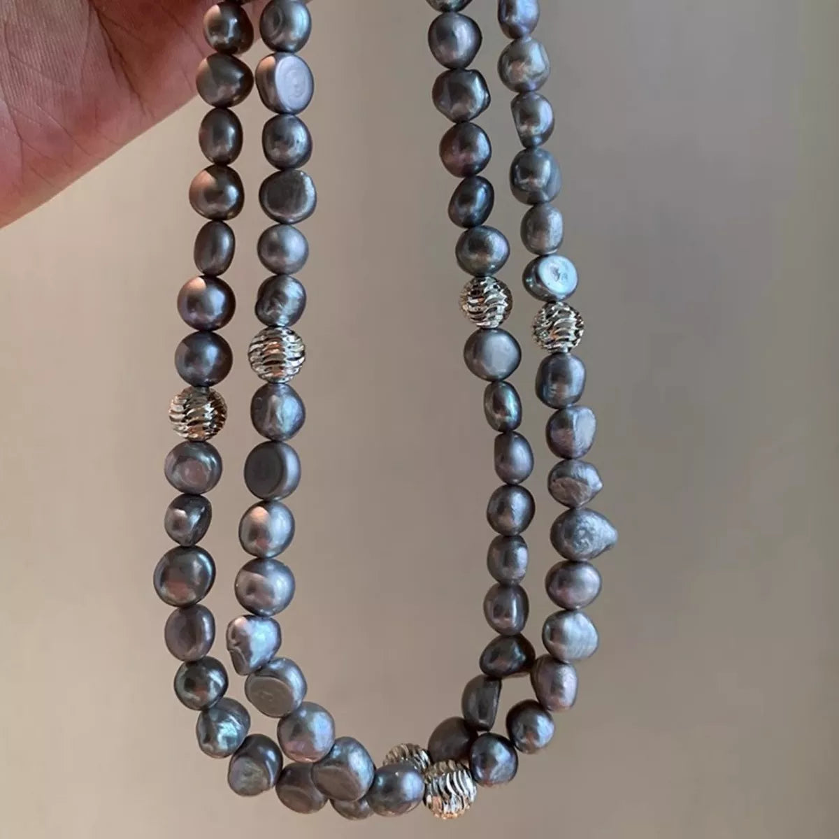 Two strands of dark pearls with silver beads against a neutral background