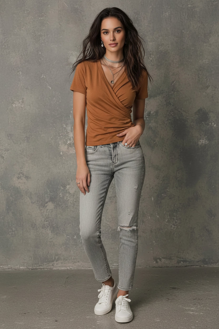 Woman wearing a brown top with layered necklaces against a gray background