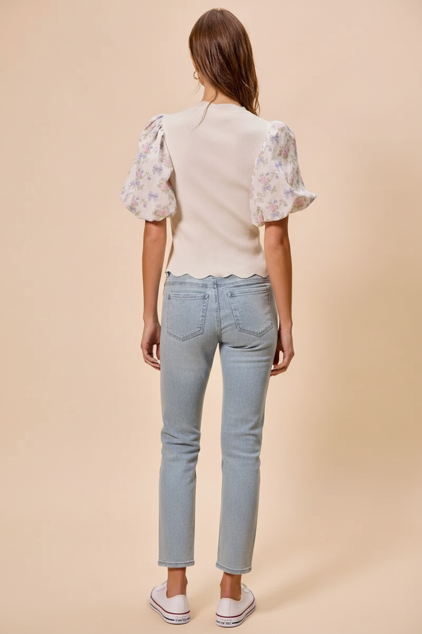 Rear view of a cream knit top with sheer floral puff sleeves and scalloped hem