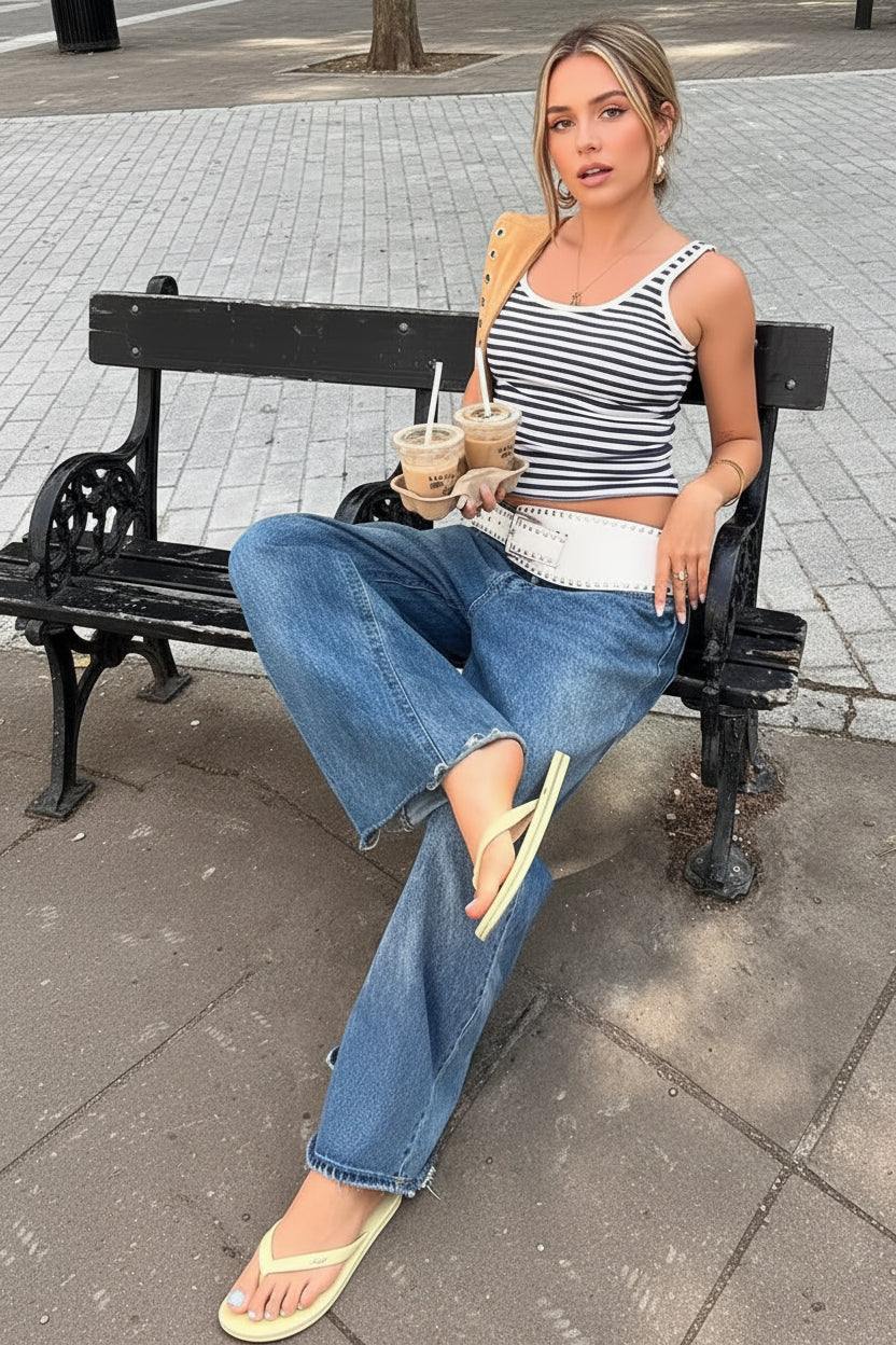 Woman sitting on a bench holding iced drinks, wearing a striped top and jeans.