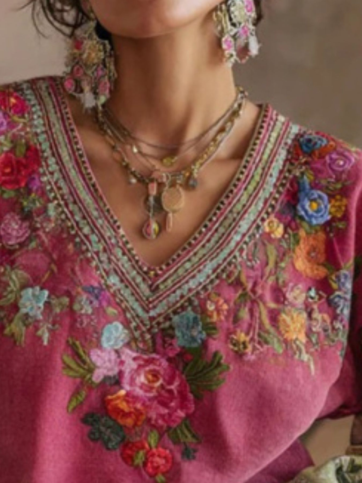 Close-up of a person wearing a pink embroidered top with floral patterns, colorful jewelry, and earrings.