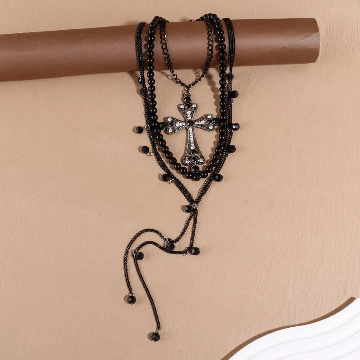 Multi-layered black beaded necklace with a cross pendant on a beige background