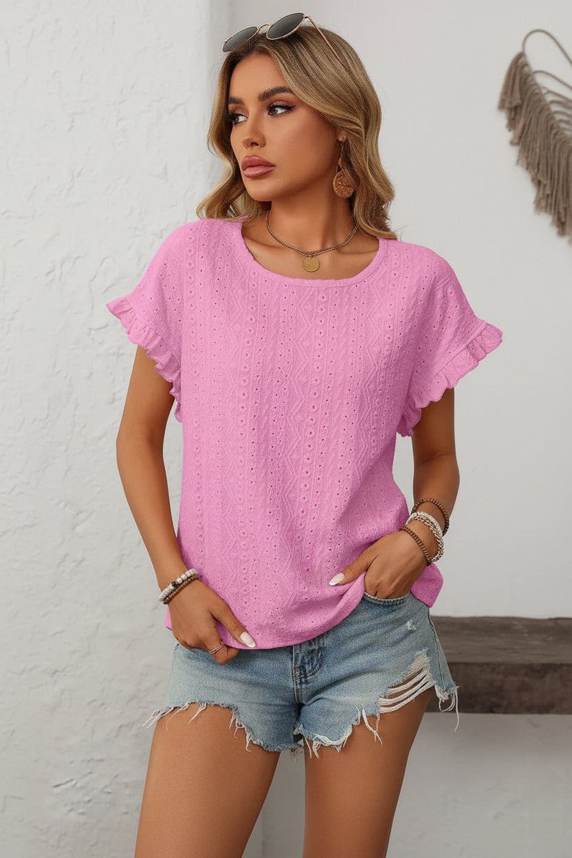 Woman wearing a pink blouse with ruffled sleeves against a white wall.