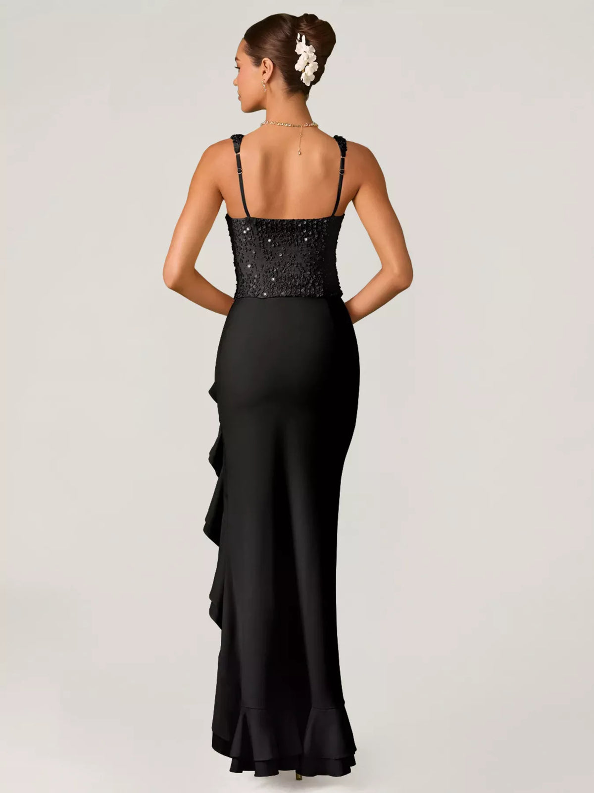 Woman wearing a black evening gown with a floral hair accessory on a white background