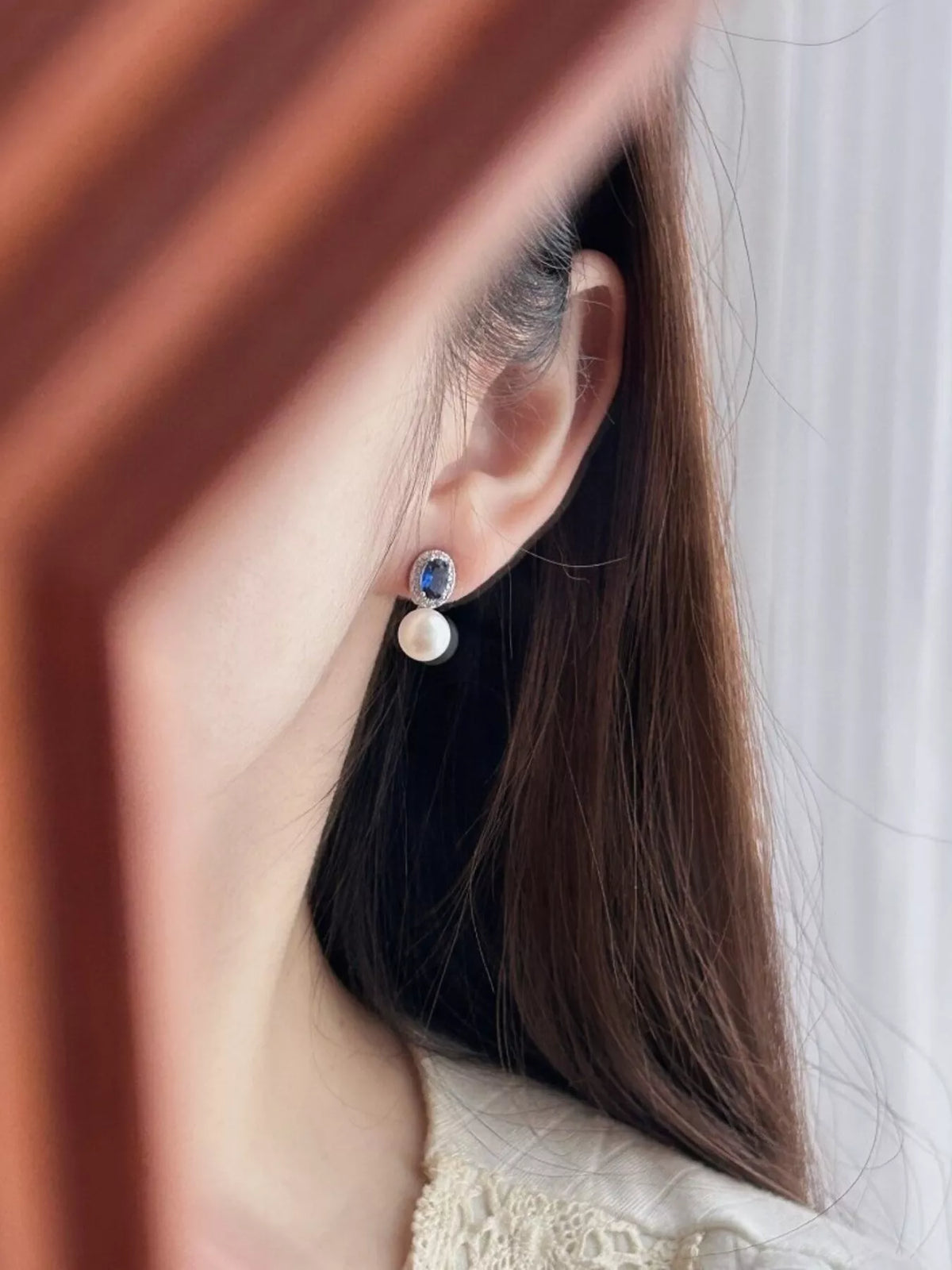 Close-up of an ear wearing a pearl earring with a blue gemstone.