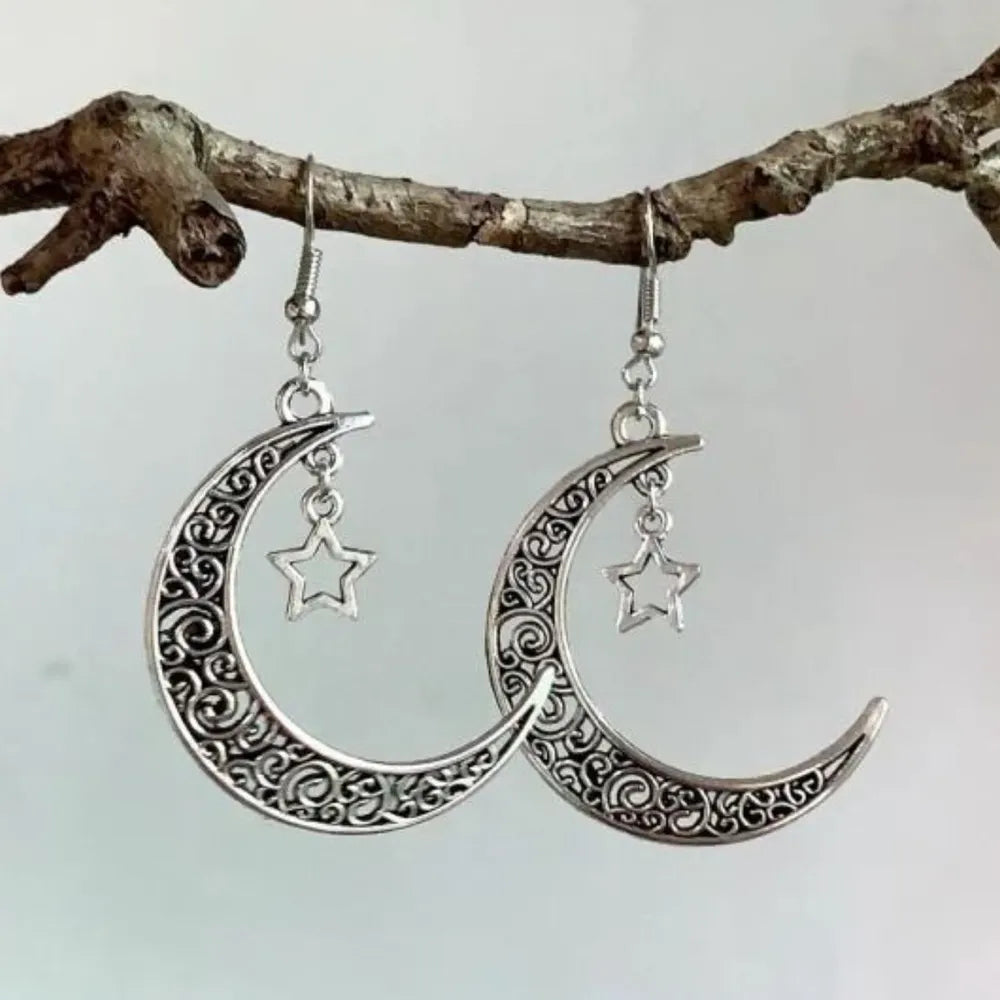 Silver crescent moon and star earrings hanging on a branch with a light background