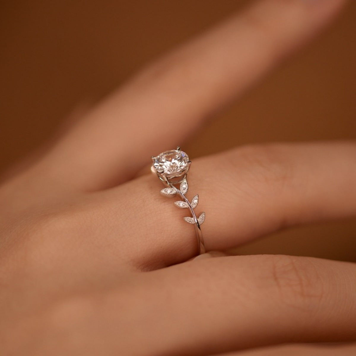 Silver ring with a diamond on a person's finger against a brown background