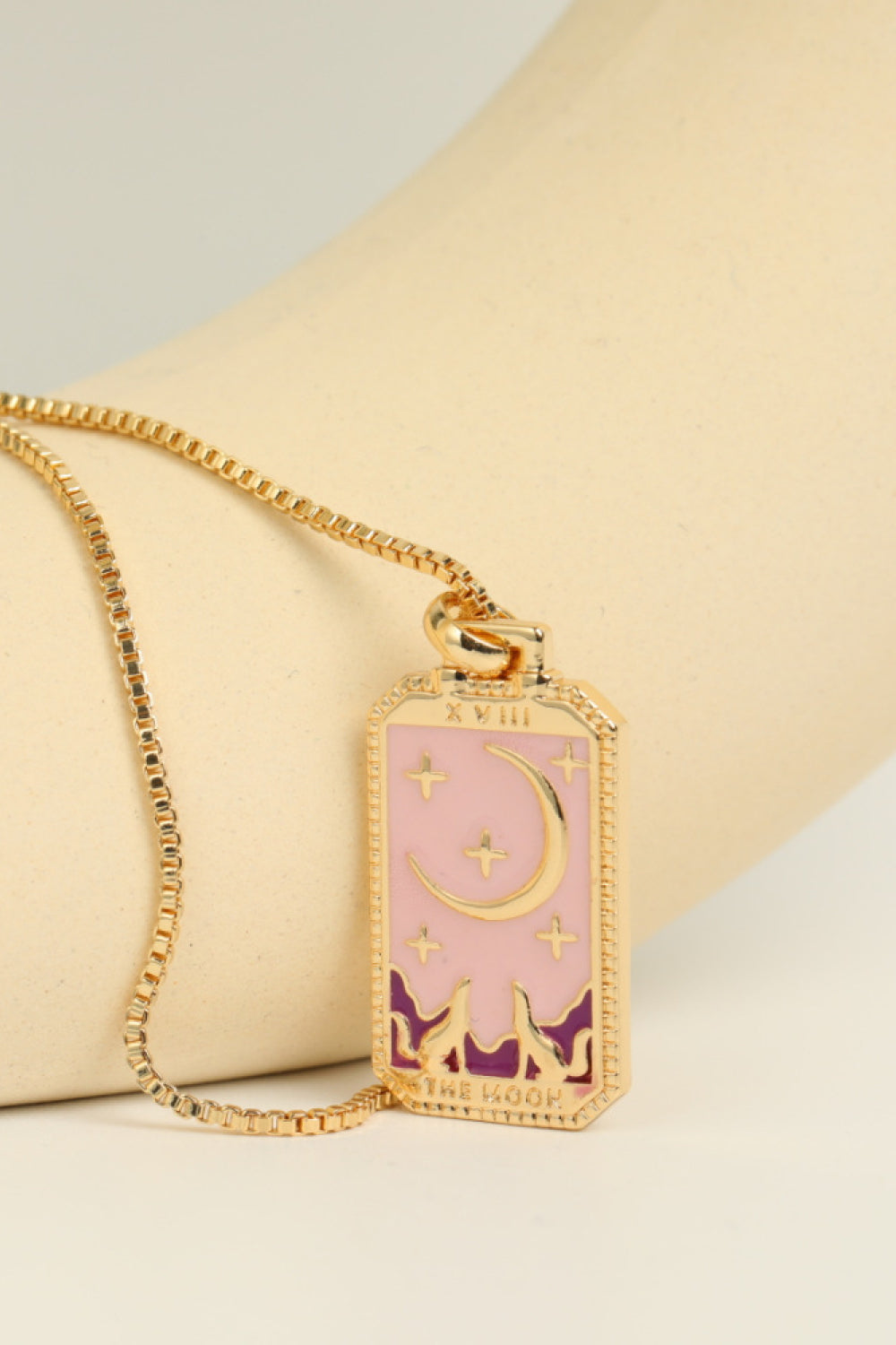 Necklace with a pink pendant featuring celestial designs on a beige surface.
