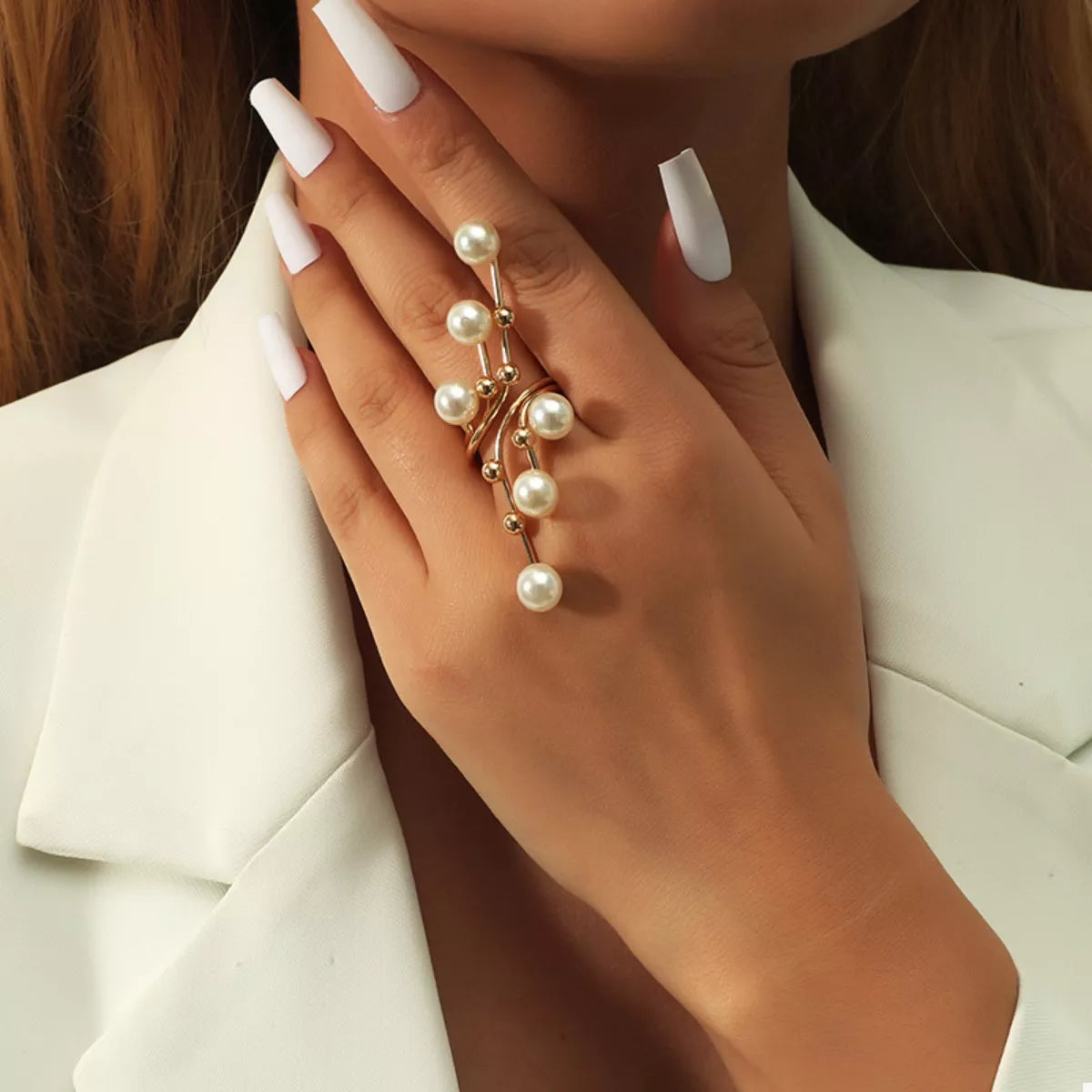Close-up of a hand wearing a gold ring with pearls against a neutral background