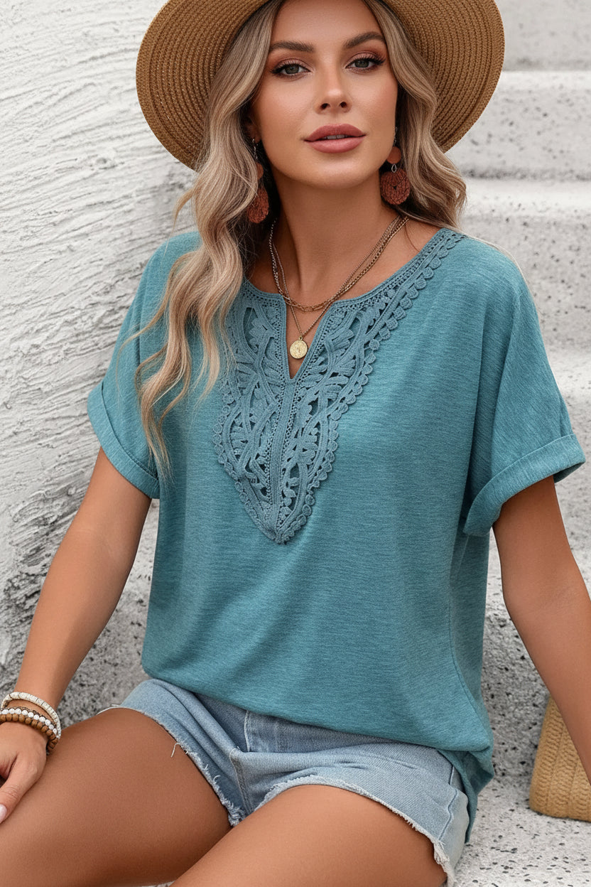 Woman wearing a blue lace-trimmed top and denim shorts sitting on a stone surface.