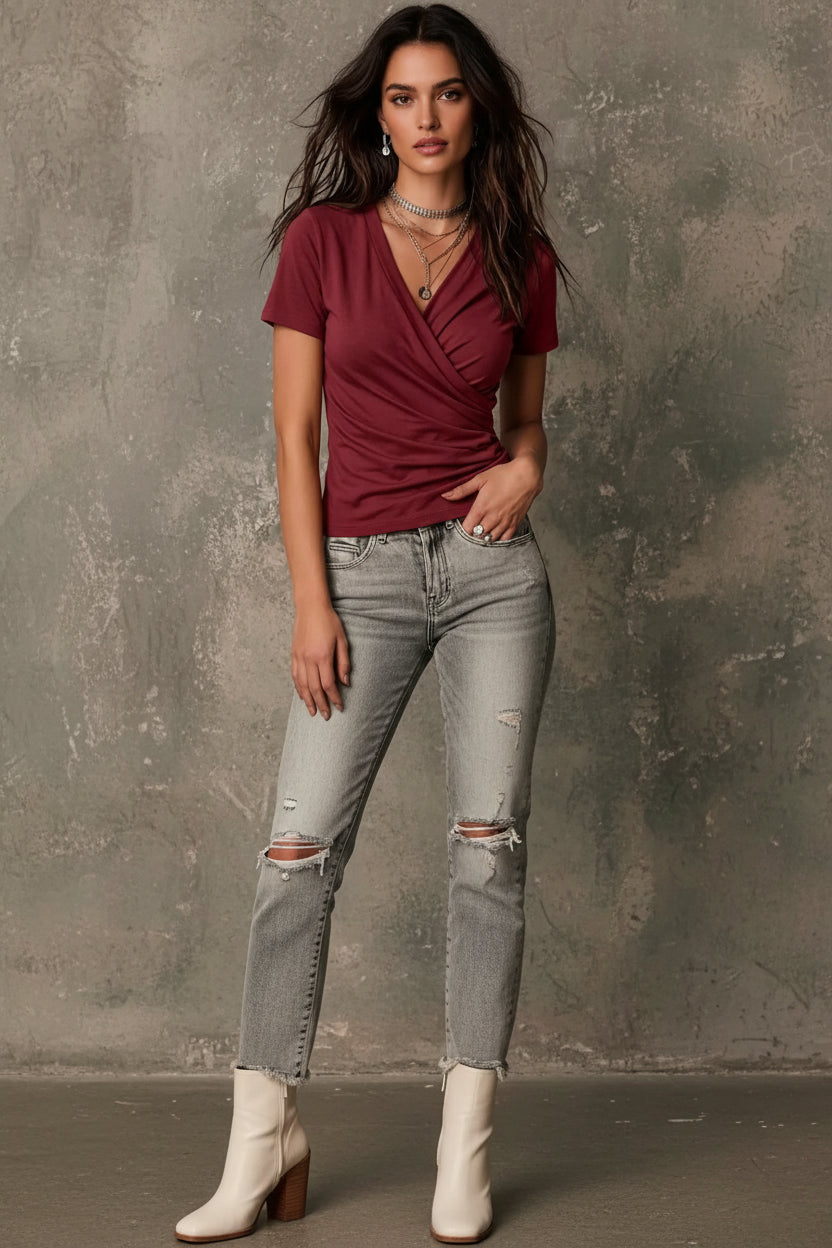 Woman wearing a burgundy wrap-style top with layered necklaces against a neutral background