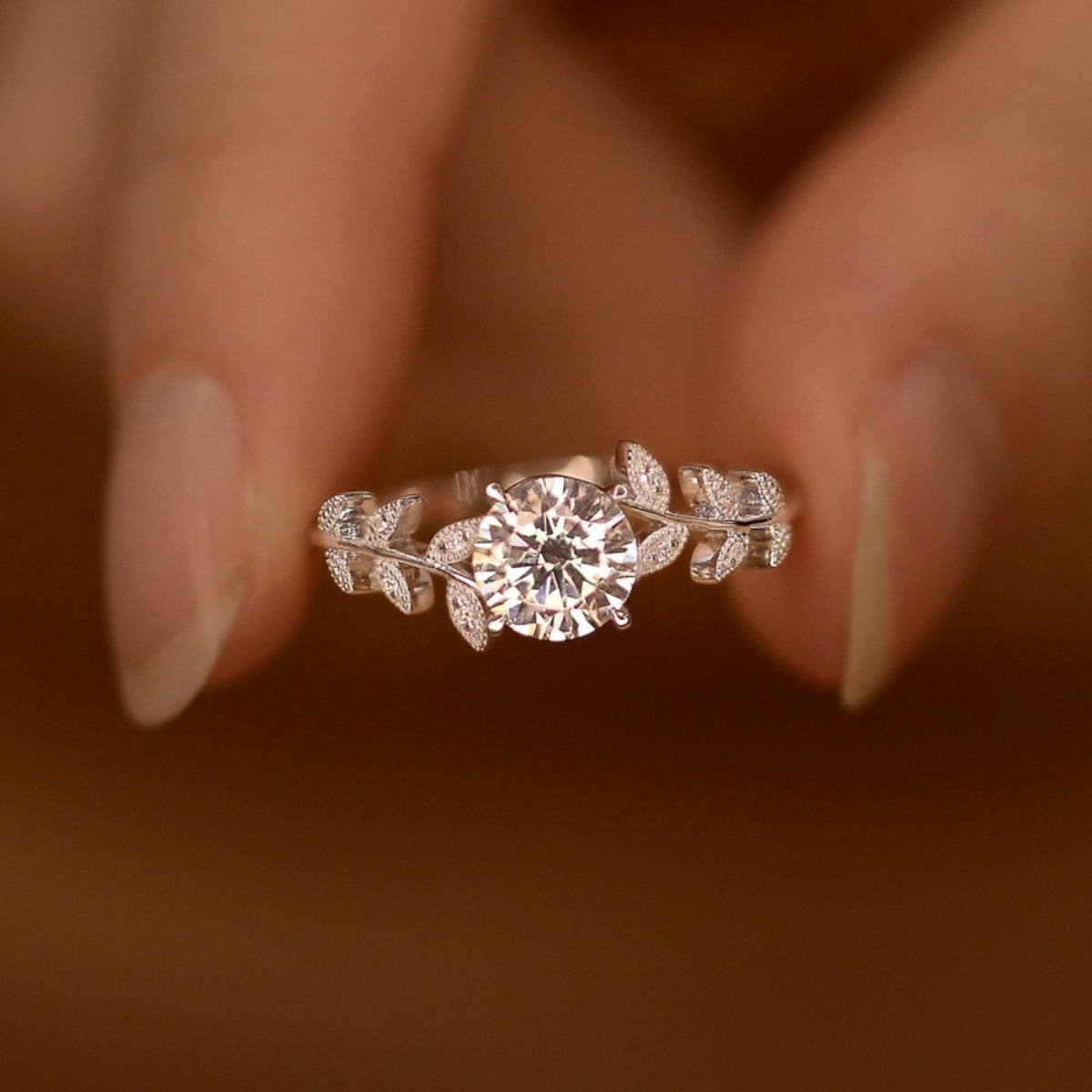 Diamond ring with leaf design on a finger against a blurred background