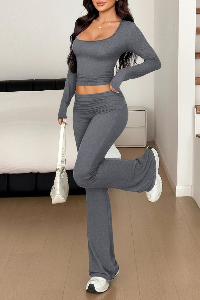 Woman in gray athletic outfit posing in a room with a couch and staircase.