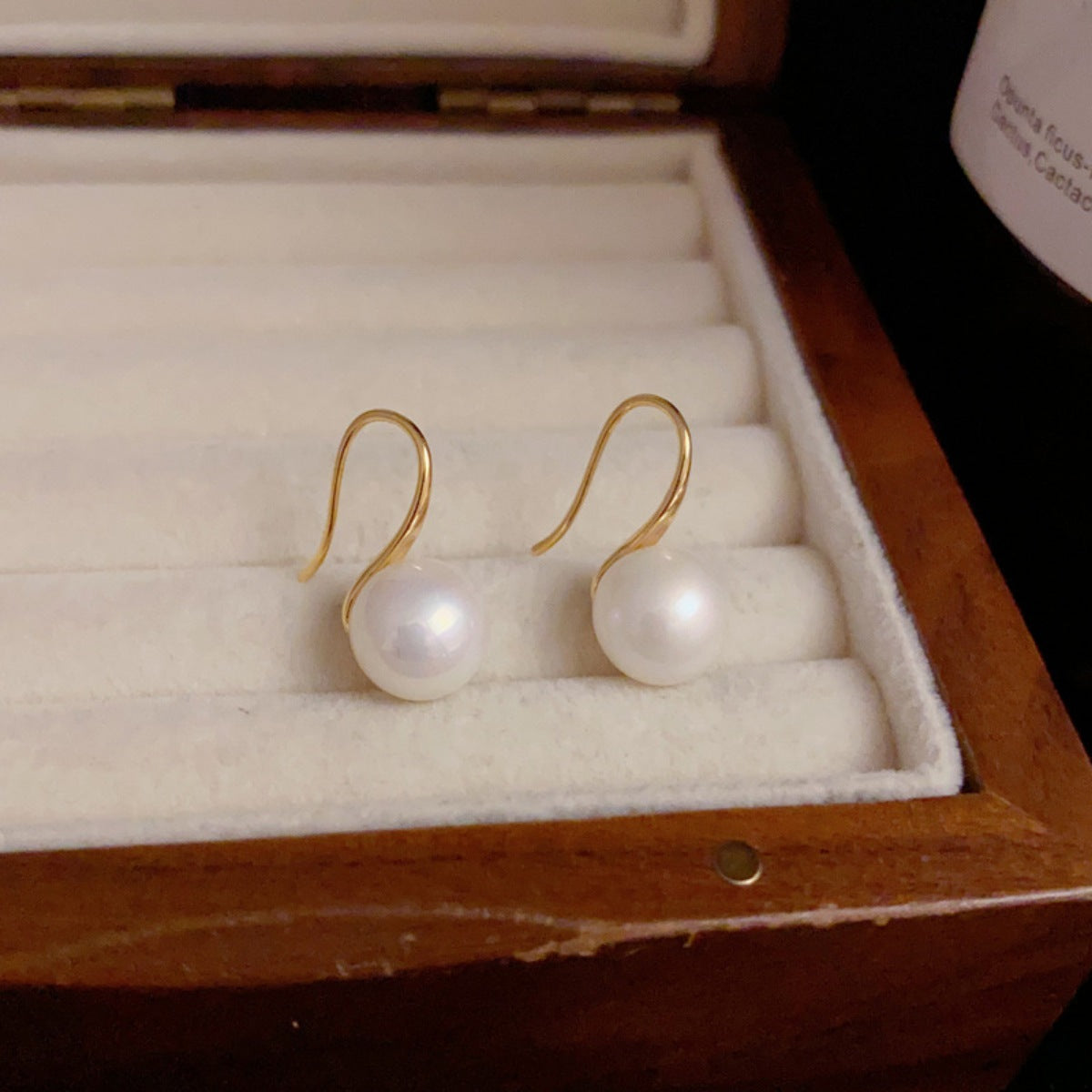 Pearl earrings with gold hooks in a wooden jewelry box.