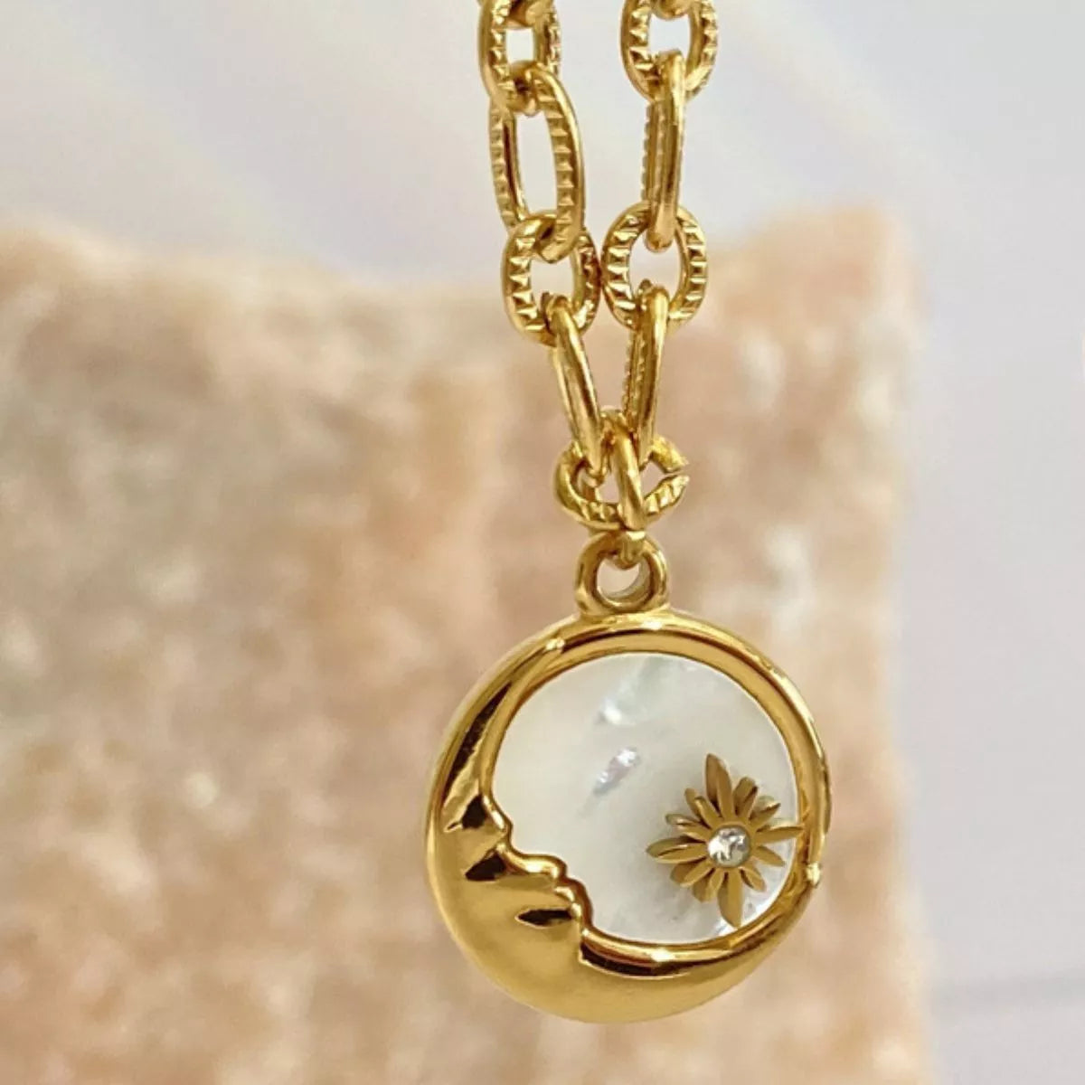 Gold necklace with a pendant featuring a moon design and a small flower on a beige background