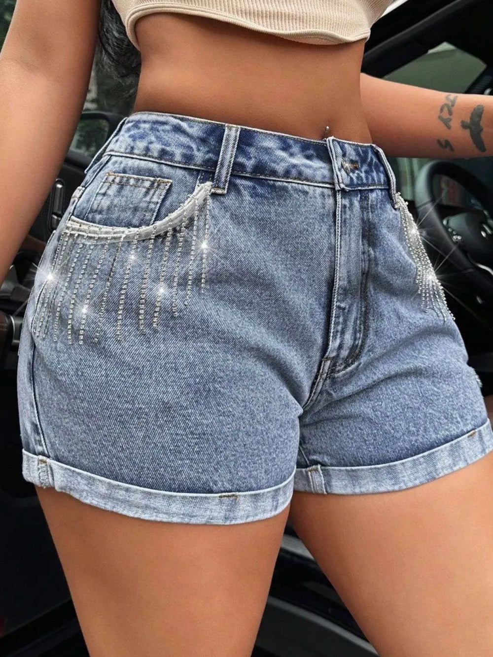 Person wearing high-waisted denim shorts with rhinestone details.