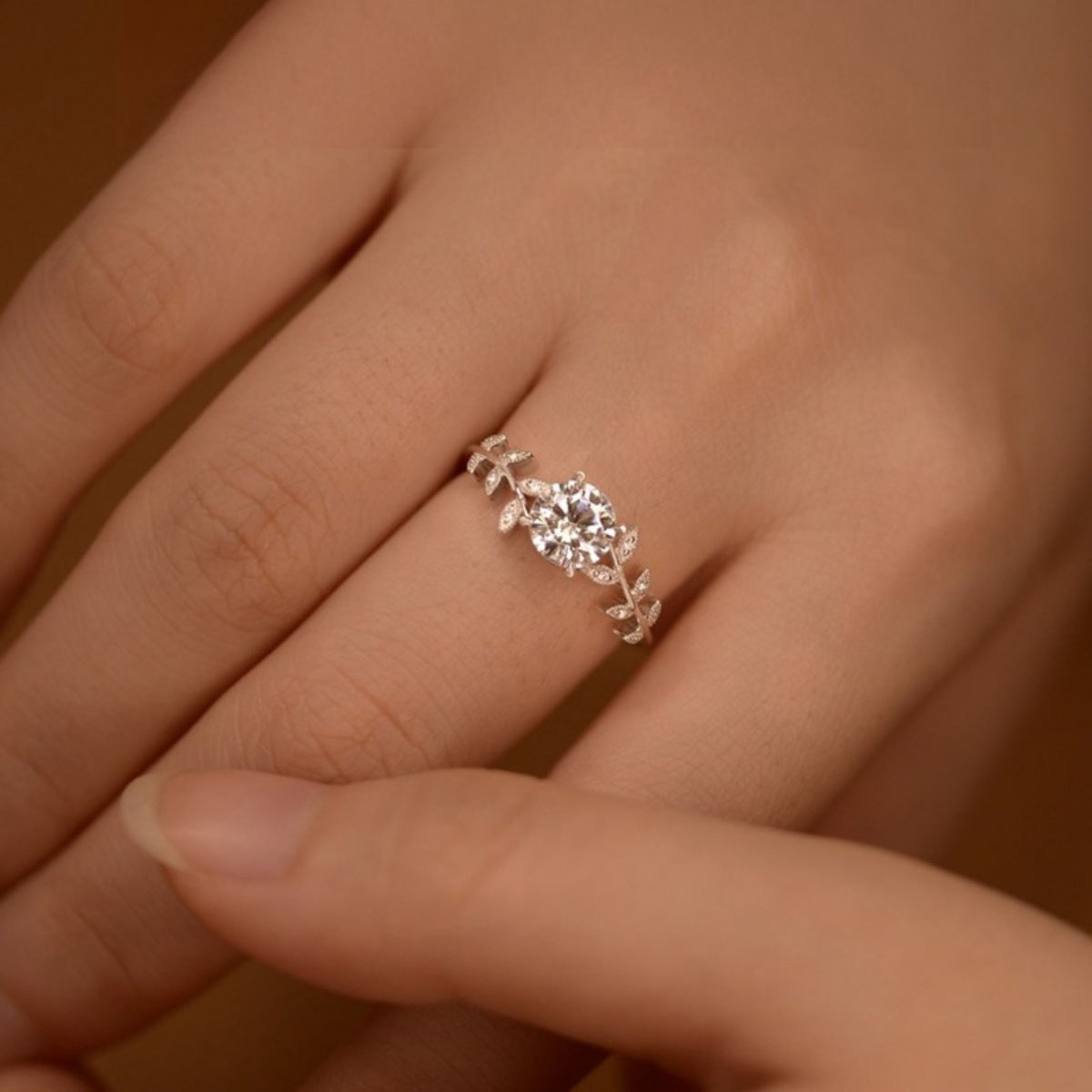 Silver ring with a diamond on a person's finger against a neutral background