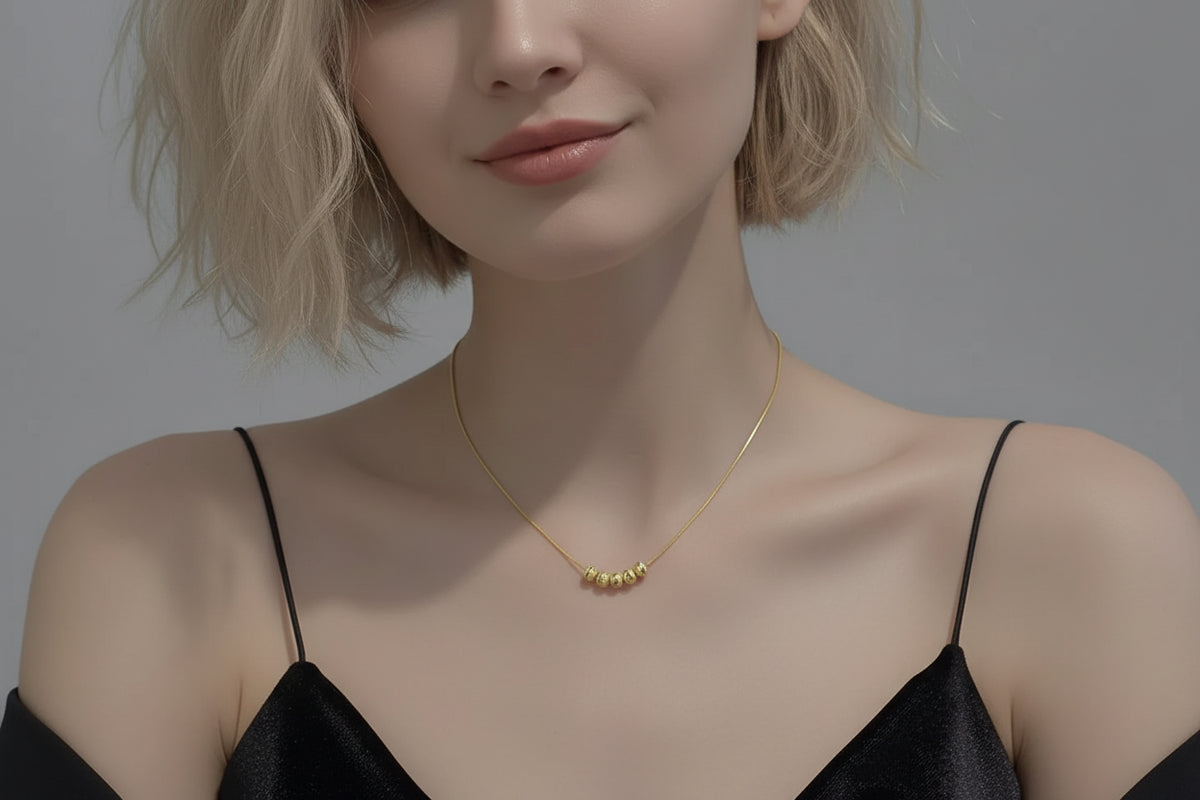 Gold necklace being worn on a person's neck with a neutral background