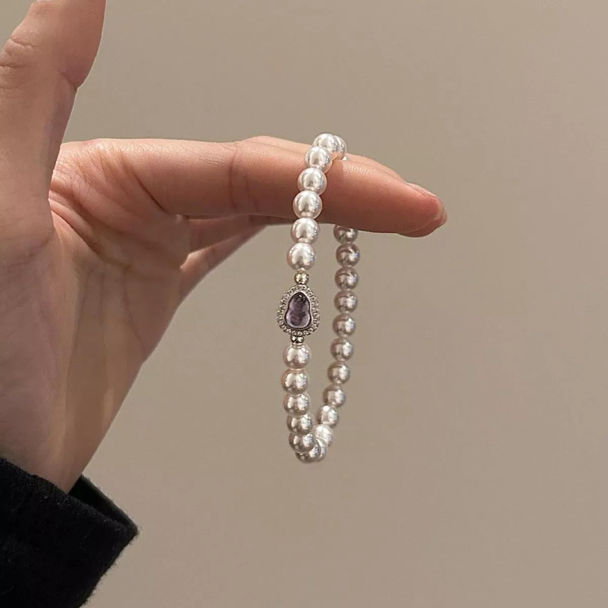 Pearl bracelet with a purple gemstone held by a hand against a neutral background