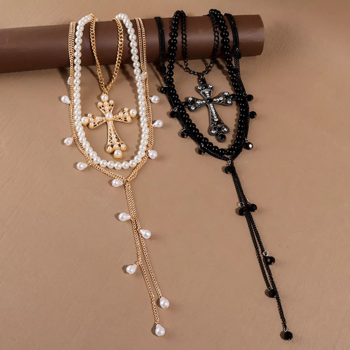 Two necklaces with crosses, one gold and one black, on a brown background.