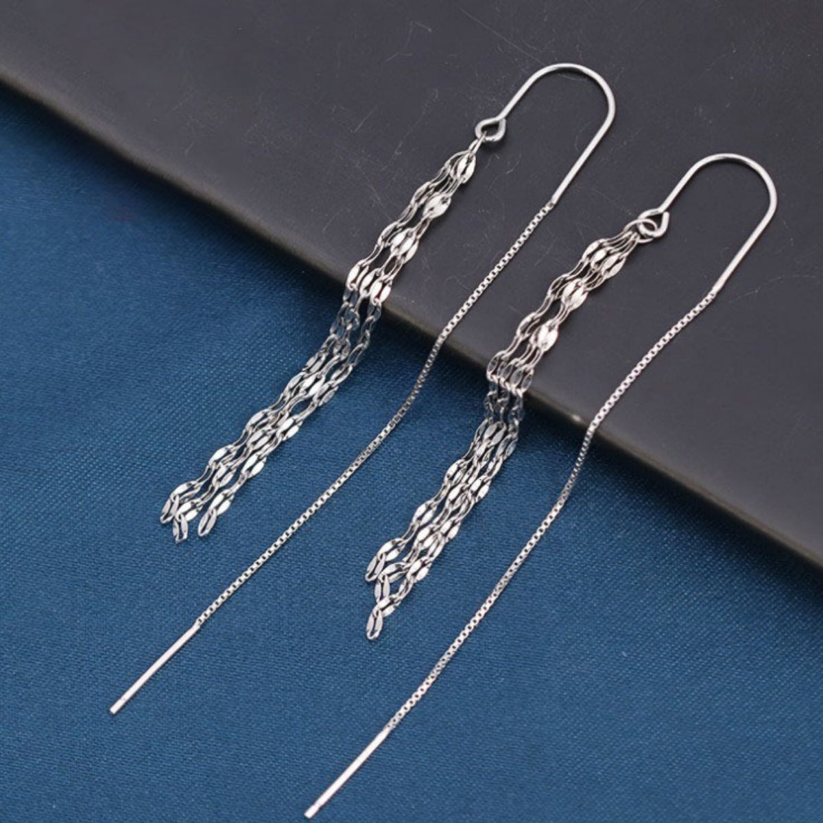 Silver chain earrings on a dark surface with a blue background