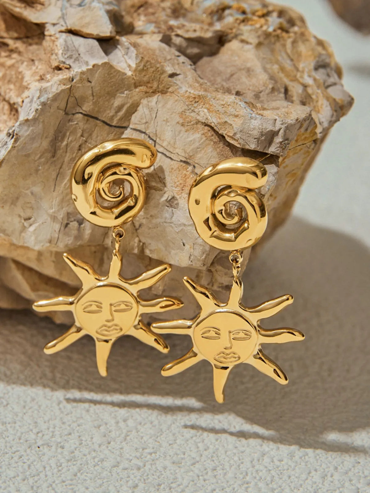Gold sun-shaped earrings on a textured stone surface